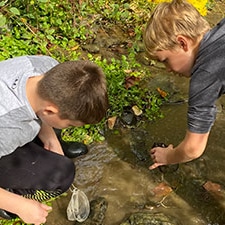 Two young students collect macroinvertebrates from a stream.