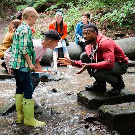 A teacher and young students exploring a stream.